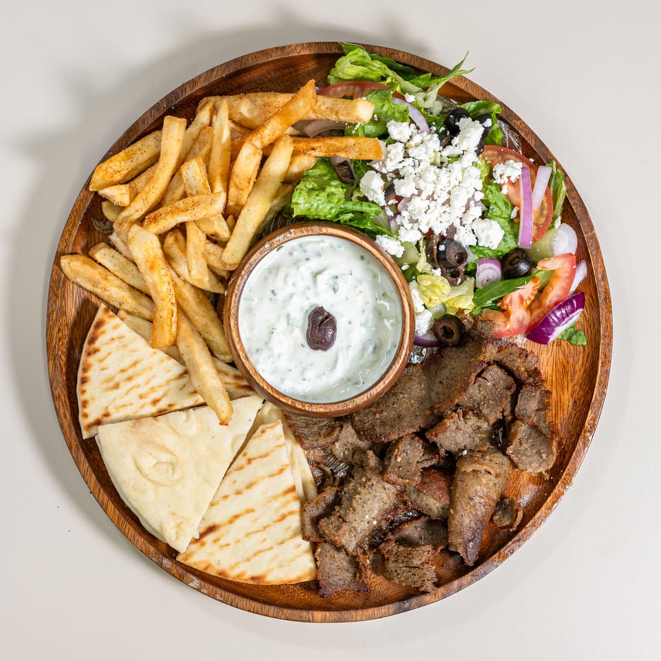 Delicious Greek platter featuring gyro meat, crispy fries, pita bread, fresh salad, and creamy tzatziki.