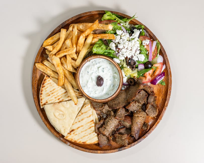 Delicious Greek platter featuring gyro meat, crispy fries, pita bread, fresh salad, and creamy tzatziki.