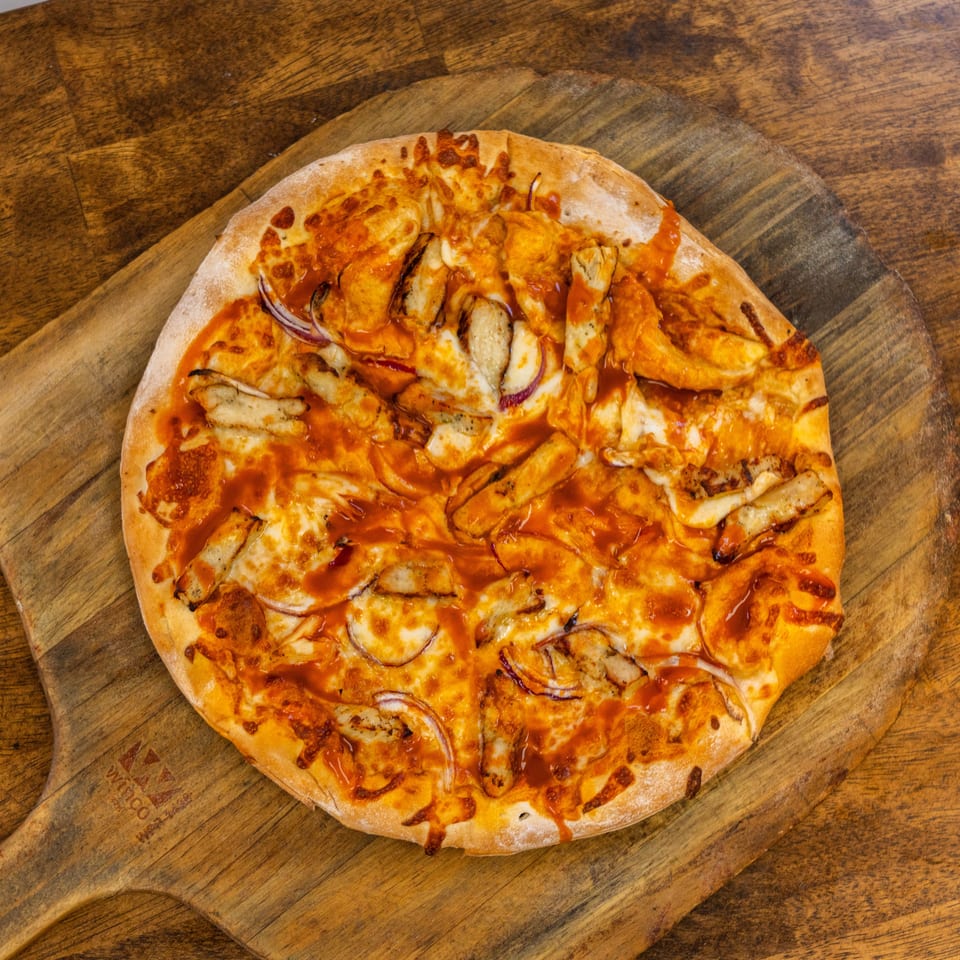 A BBQ chicken pizza with red onions and sauce on a wooden pizza peel.