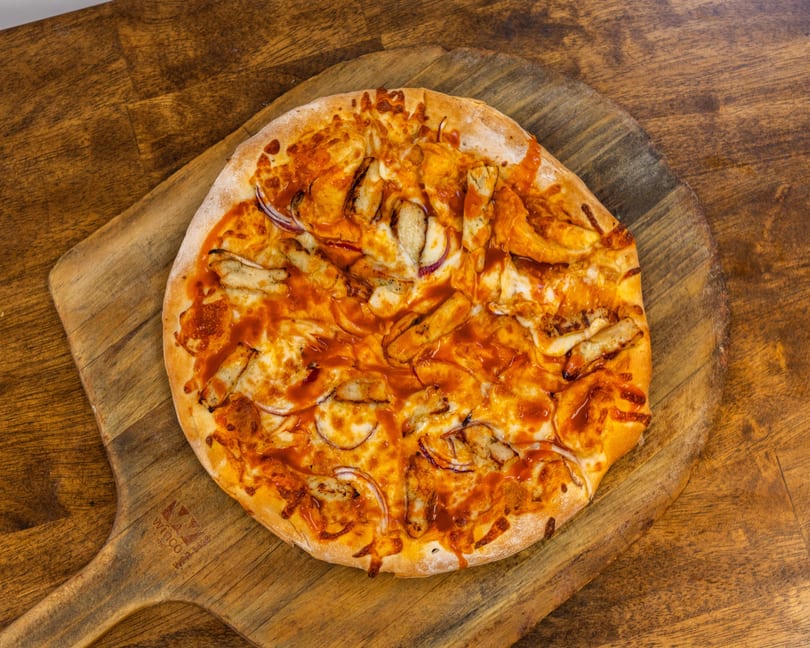 A BBQ chicken pizza with red onions and sauce on a wooden pizza peel.