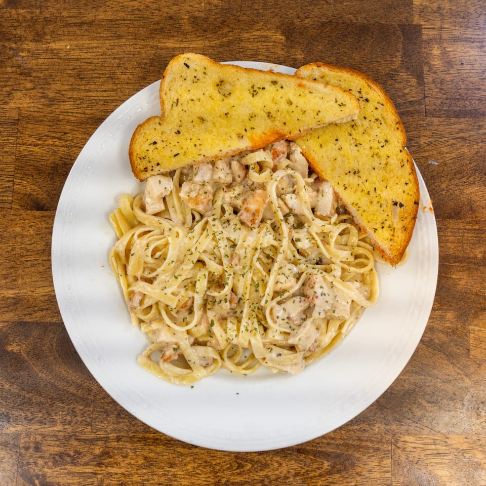 Creamy fettuccine alfredo with chicken and shrimp, garnished with parsley, served with garlic bread.