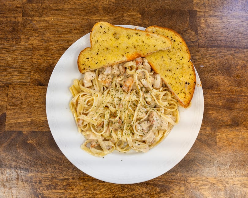 Creamy fettuccine alfredo with chicken and shrimp, garnished with parsley, served with garlic bread.