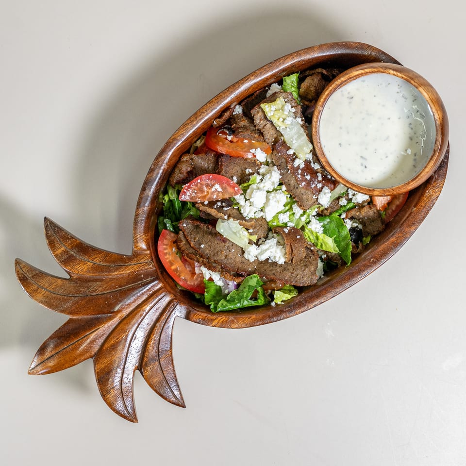 Gyro meat salad with feta, tomatoes, and lettuce in a pineapple-shaped wooden bowl with dressing.
