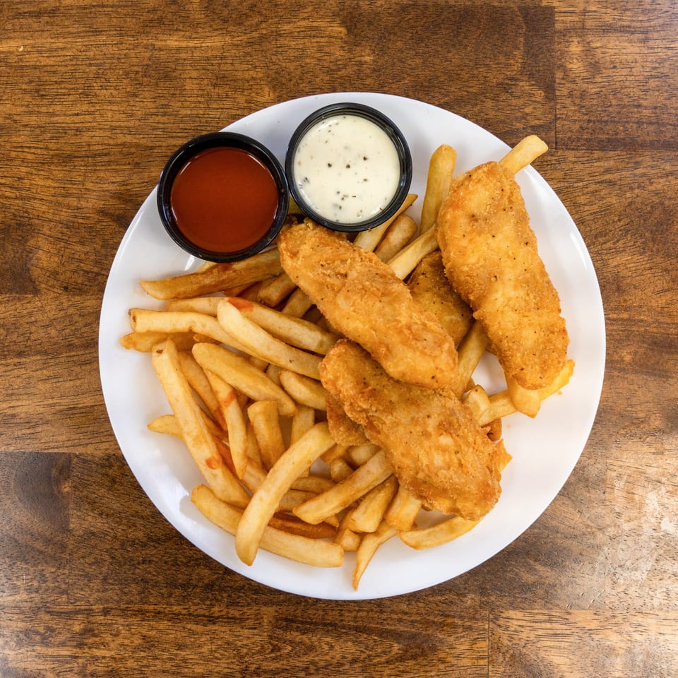 A white plate of golden-brown fish and chips with ketchup and tartar sauce on a wooden table.
