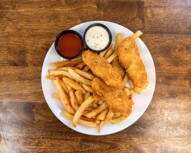 A white plate of golden-brown fish and chips with ketchup and tartar sauce on a wooden table.