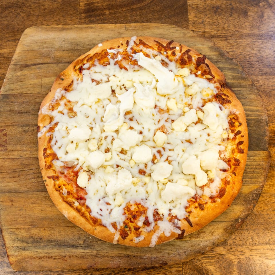 A cheese pizza with large chunks of white cheese and melted mozzarella on a wooden pizza peel.