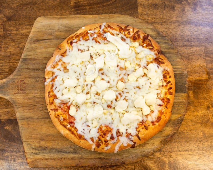 A cheese pizza with large chunks of white cheese and melted mozzarella on a wooden pizza peel.