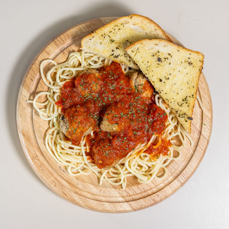 Spaghetti and meatballs with red sauce and parsley, served with two slices of garlic bread on a wooden board.