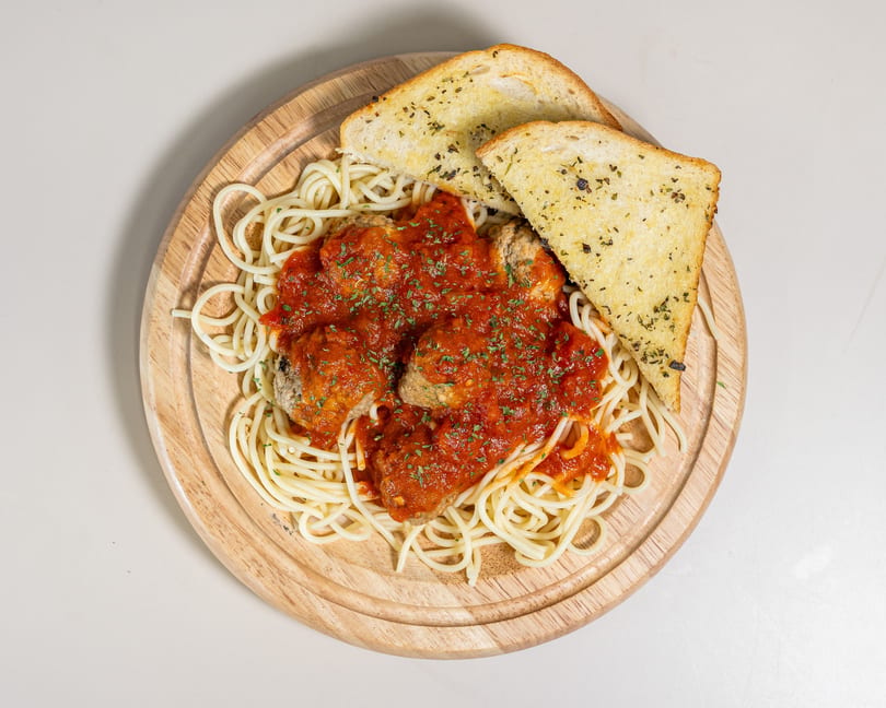Spaghetti and meatballs with red sauce and parsley, served with two slices of garlic bread on a wooden board.