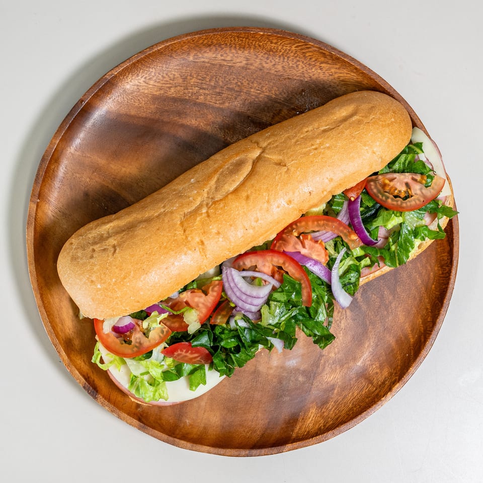 Long sub sandwich filled with fresh lettuce, tomatoes, red onions, and deli meats on a wooden platter.