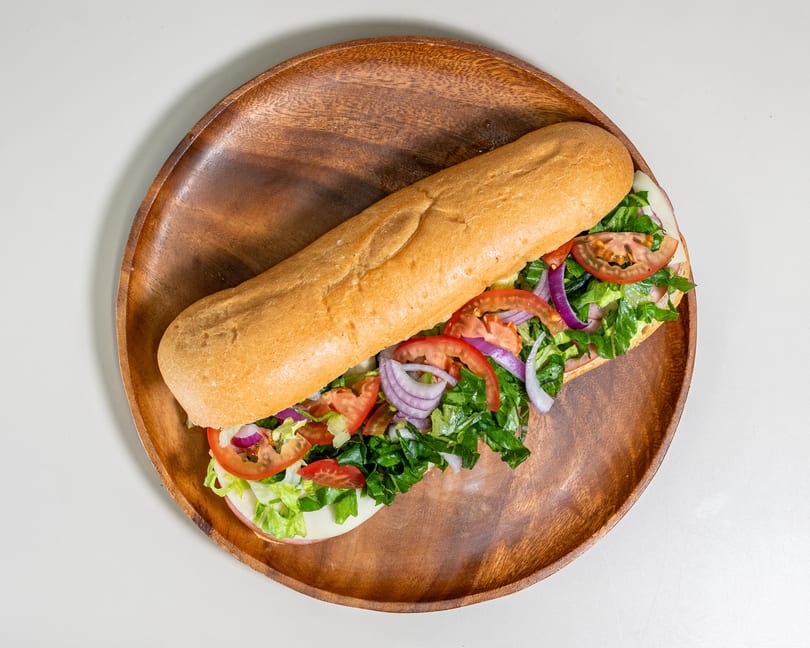 Long sub sandwich filled with fresh lettuce, tomatoes, red onions, and deli meats on a wooden platter.